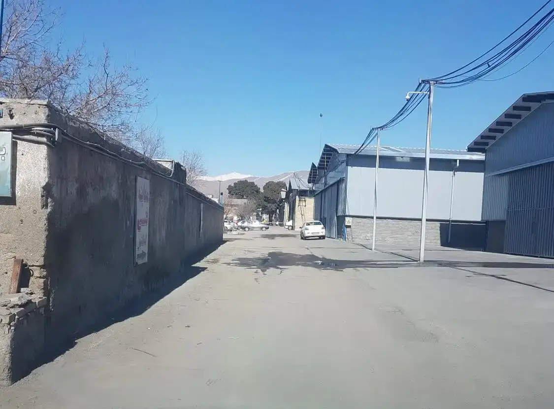 جاده‌ی دسترسی به مرکز از نگاه راننده: دیوار بلند در سمت چپ و سوله‌ها در سمت راست
